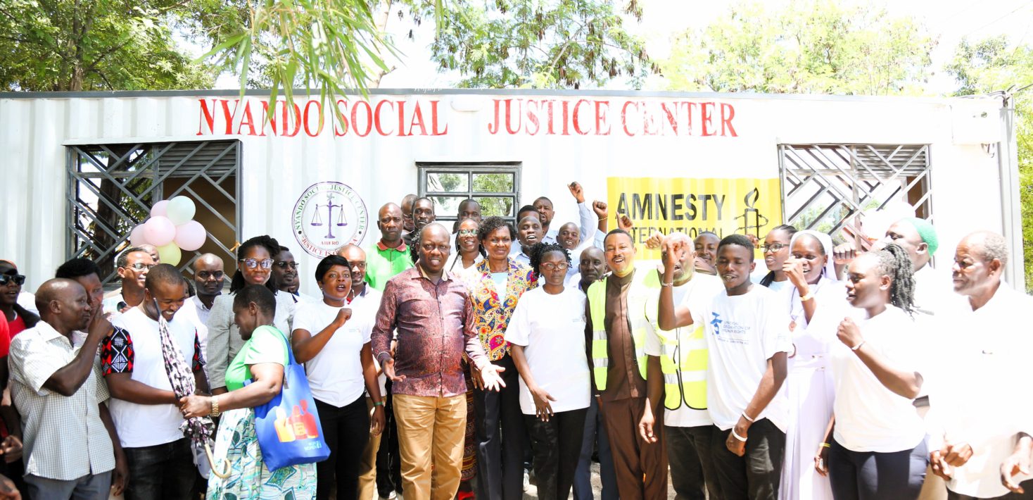 A group of people smiling on a sunny day behind a metal container with words writtern Nyando Justice Centre